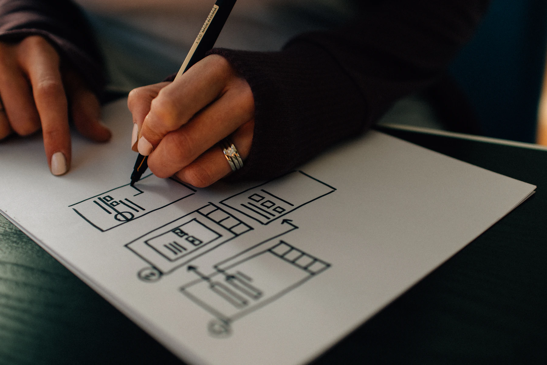 Hands sketching interface wireframes on a sheet of paper